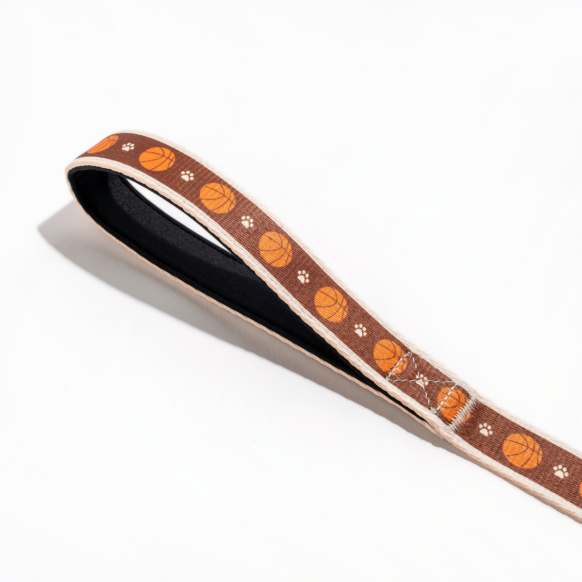 Close-up of the Floofball basketball dog leash padded handle with black lining and orange basketball print.