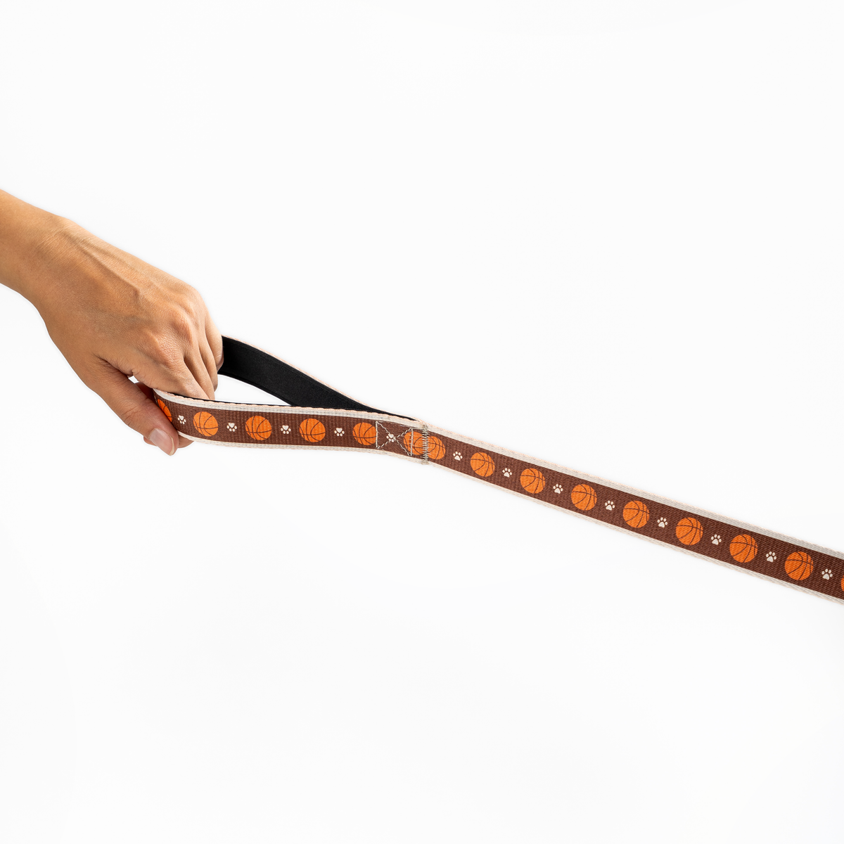 Floofball basketball dog leash held horizontally, showing the brown and orange basketball and paw print pattern.