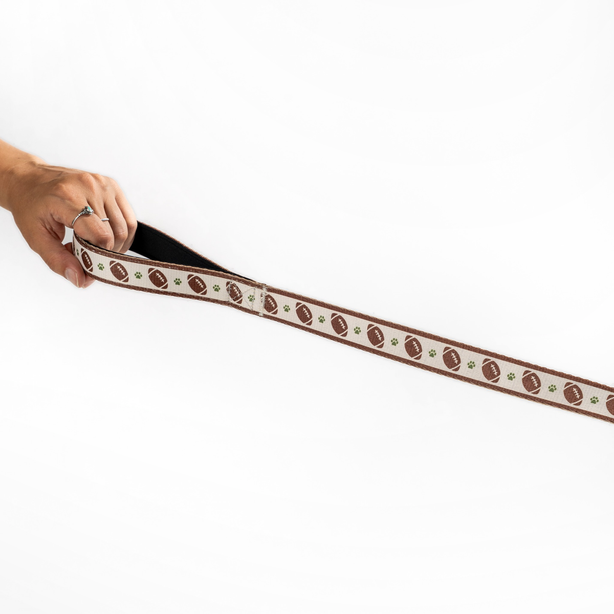 Close-up of the Floofball football dog leash held in hand, showing its patterned webbing and reinforced construction.
