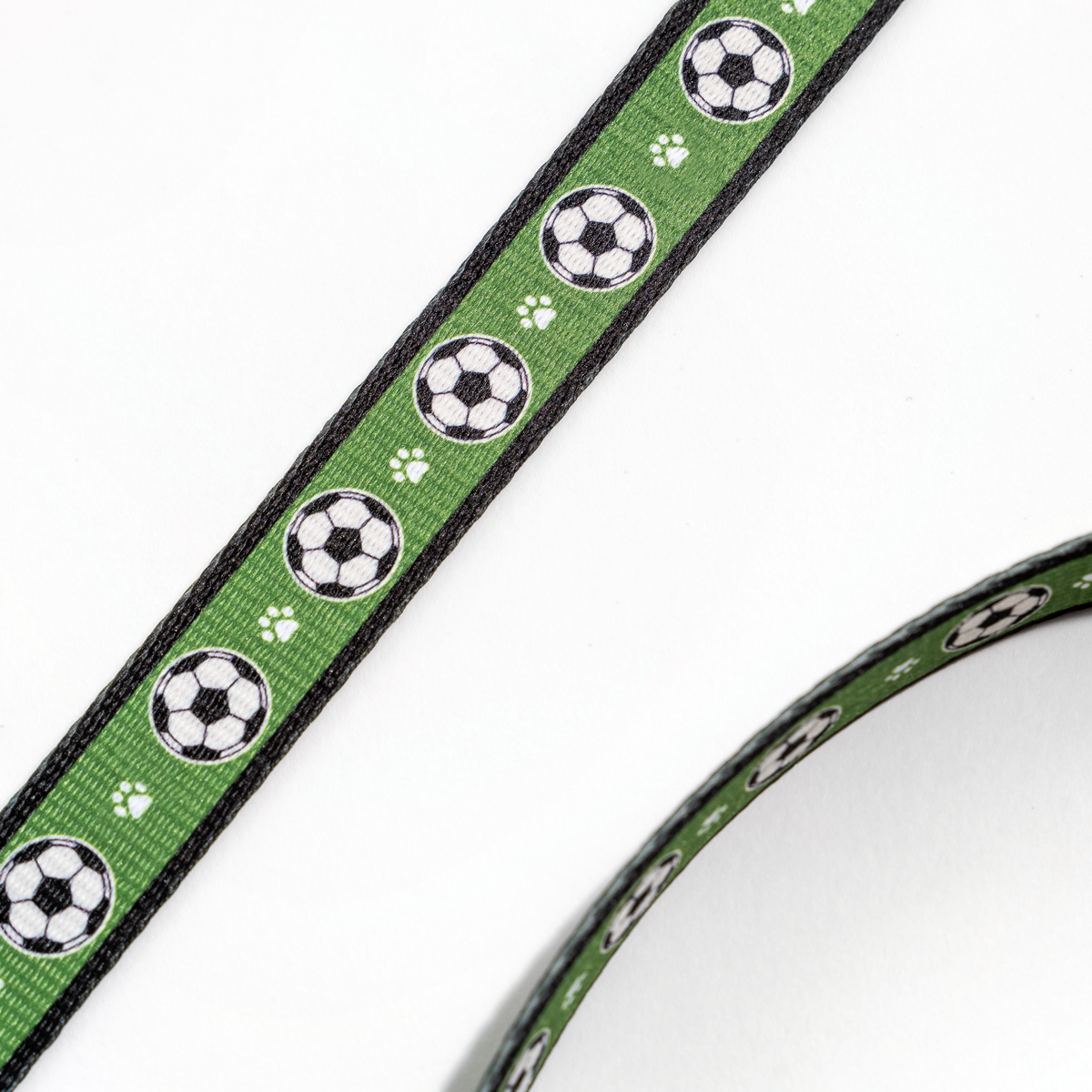 Close-up of the Floofball soccer dog leash featuring repeating soccer balls and paw prints on green webbing.