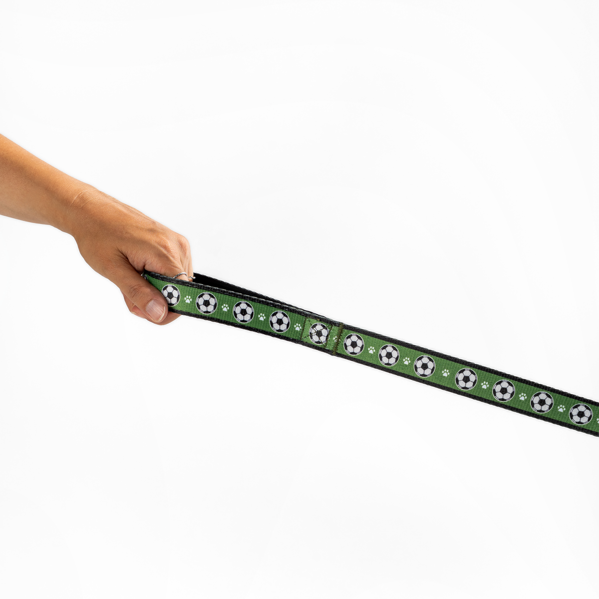Floofball soccer dog leash held horizontally, showing the green soccer ball and paw print pattern with black trim.